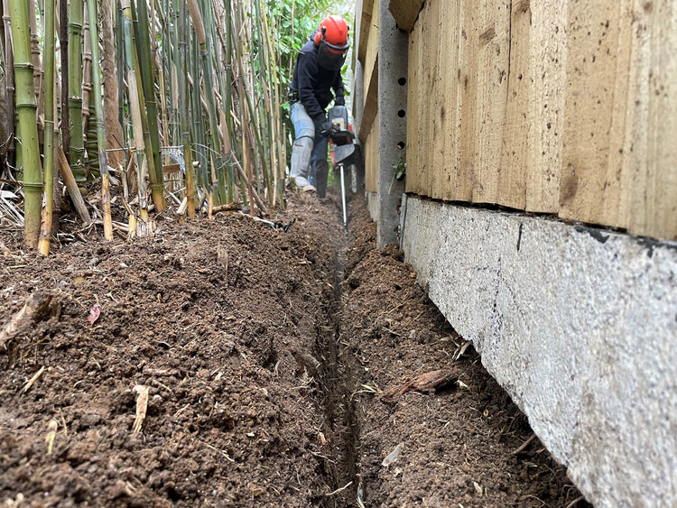 Image of a person next to a fence using a soil saw to dig a trench.